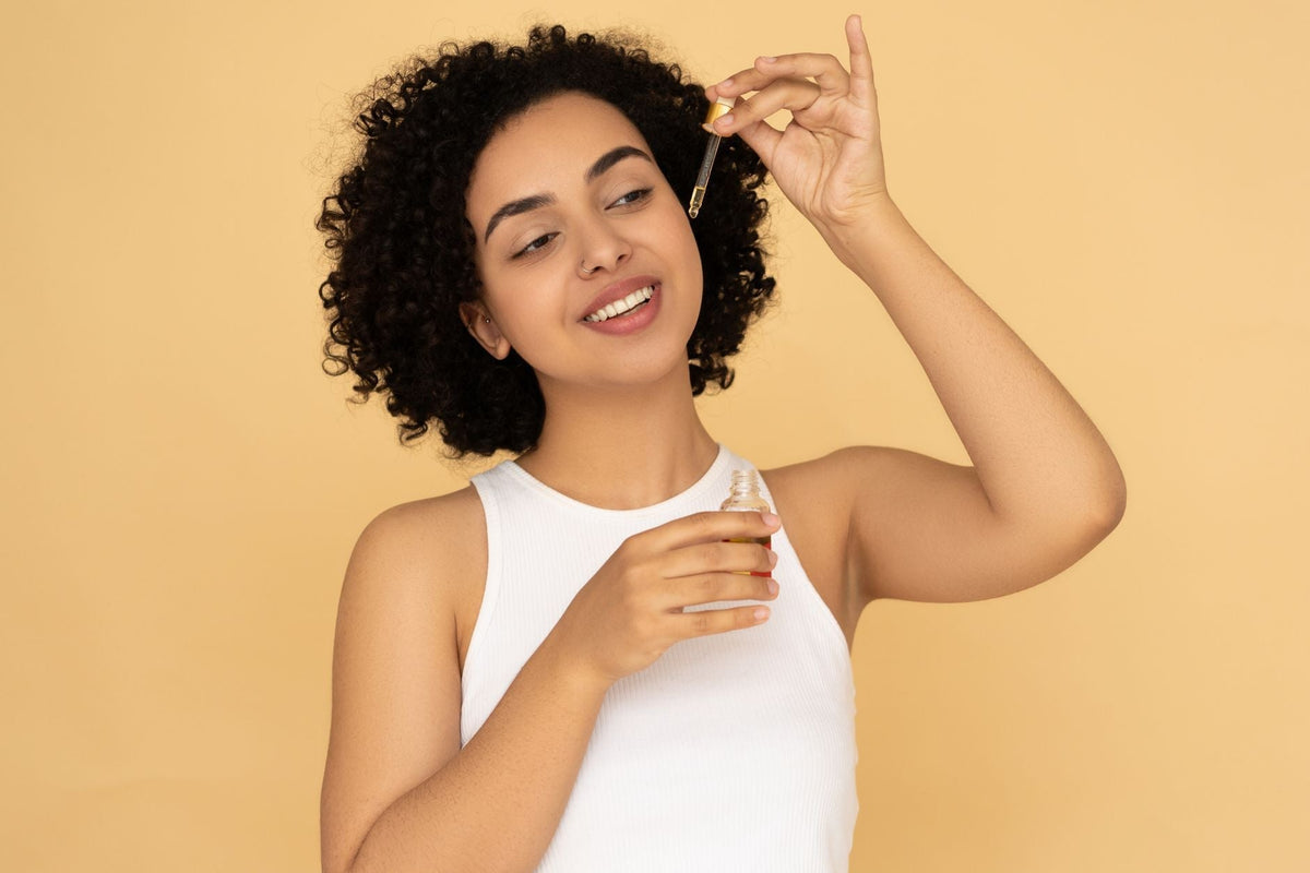 A woman with curly hair applies essential oil on her skin, promoting wellness and skincare.