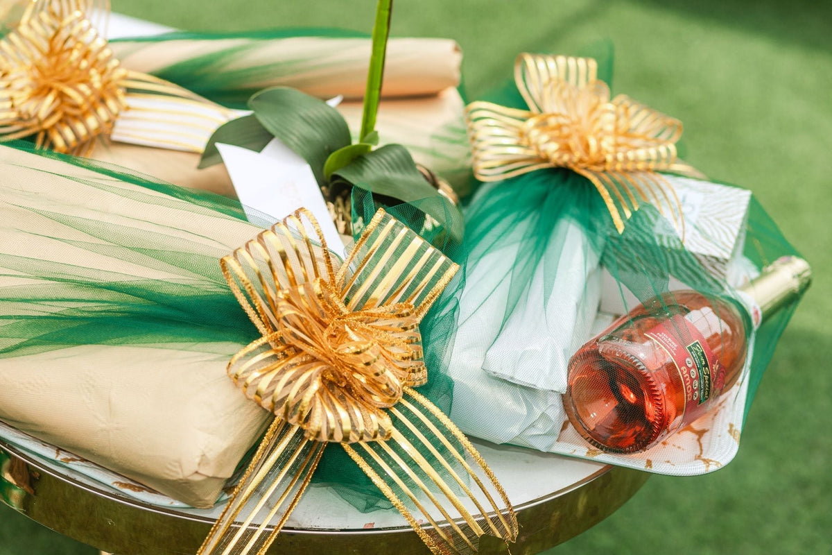 A close-up of beautifully wrapped gifts with green and gold decorations and a bottle of rose wine.